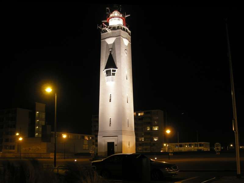 A captivating nighttime view of the Noordwijk lighthouse, illuminated against the dark sky. The beacon atop the lighthouse casts a powerful beam of light into the night, guiding ships safely along the coastline. The surrounding landscape is bathed in a soft glow, creating a serene ambiance. This enchanting scene captures the nocturnal beauty and maritime importance of the Noordwijk lighthouse, showcasing its role as a guardian of the sea under the cover of darkness.